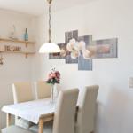 Esszimmer mit Tisch, Stühlen, Wandbild und Deckenleuchte. An der Wand hängt ein Bild mit Orchideen.