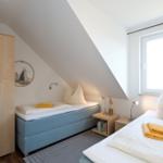 Zimmer mit zwei Betten, Schrank und Fenster unter Dachschrägen.