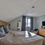 Schlafzimmer mit Bett, Kleiderschrank und TV. Fenster mit Vorhängen und Spiegel.