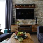 Wohnzimmer mit Fernseher, Holztisch und Steinwand
