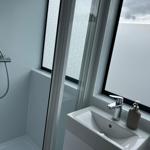 Badezimmer mit Dusche, Waschbecken und Fenster mit getöntem Glas.