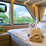 Schlafzimmer mit Blick auf Wasser und Ufervegetation. Bett mit Handtuchschwanen.