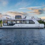 Ein weißes Hausboot mit großem Deck und Fenstern liegt auf ruhigem Wasser.