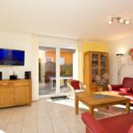 Wohnzimmer mit rotem Sofa, Holzmöbeln und Fernseher. Durchgang zur Terrasse.