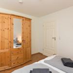 Schlafzimmer mit Holzschrank, Bett und Stuhl. Wandbild und Tür sind sichtbar.