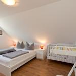 Zimmer mit Doppelbett, Kinderbett und Schrank an der Wand.
