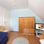 Ein Raum mit blauer Wand, Holzmöbeln und einem Sofa. Fernseher und Rattanstühle sind vorhanden.