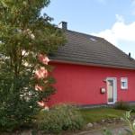 Rotes Haus mit Dach und Eingang. Umgeben von Grünflächen und Bäumen.