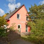 Rotes Haus mit Gartenzaun und Bäumen unter blauem Himmel.