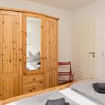 Schlafzimmer mit Holzschrank, Bett und zwei roten Stühlen.