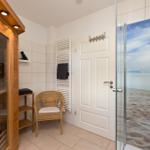 Dusche mit Strandmotiv, Sauna und Wickerstuhl im Badezimmer.