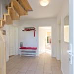 Hausflur mit Holztreppe, roter Sitzbank und Garderobe.
