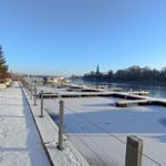 Schneebedeckter Bootssteg am Fluss mit Blick auf die Stadt
