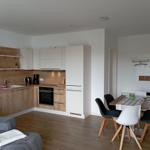 Küche mit Essbereich und Wohnbereich. Holzoptik, weiße Schränke, Esstisch mit Stühlen.