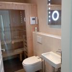 Badezimmer mit Dusche, Toilette und Waschbecken. Spiegel mit Beleuchtung.