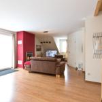 Wohnzimmer mit Sofa, Kamin und TV. Holzboden und große Glastüren.