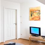 Ein Raum mit Fernseher, Spiegel und Wandbild. Tür und Stuhl sind sichtbar.