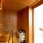 Sauna mit Holzbank, Eimer und Heizung. Tür führt in Dusche.