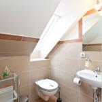 Badezimmer mit Toilette, Waschbecken und Dachfenster. Wandfliesen und Spiegel sichtbar.
