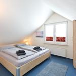 Schlafzimmer mit Doppelbett, Fenster und Schrank. Blauer Teppich und TV.