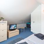 Schlafzimmer mit Bett, TV, Schrank und Kinderbett unter Dachschrägen.