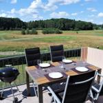 Terrasse mit Tisch, Stühlen und Grill. Blick auf Golfplatz und Wald.