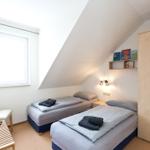 Zwei Betten, Schrank, TV und Fenster mit Vorhang in einem Dachzimmer.