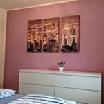 Schlafzimmer mit rosa Wand, weißem Schrank und dreiteiliger Stadtansicht