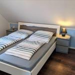Schlafzimmer mit Doppelbett, Nachttisch und Lampe. Holzfußboden und schräger Dachfirst.