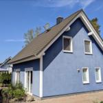 Blau gestrichenes Einfamilienhaus mit Dachterrasse und Gartenbereich unter klarem Himmel.