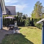 Hinterhof mit Grill, Tisch, Stühlen und Sonnenschirm. Grünfläche und Hecke umgeben den Raum.