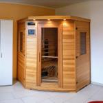 Holz-Infrarot-Sauna mit Glasfront und Bedienfeld. Weiße Schrankwand und weiße Tür im Hintergrund.