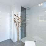 Moderne Dusche mit Glaswand, weiße Fliesen und Holzdekoration.