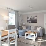 Wohn- und Essbereich mit Sofa, Tisch und Stühlen. Wandbild und Fenster sichtbar.