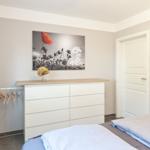 Schlafzimmer mit weißem Schrank, Bett und Wandbild mit Mohnblume.