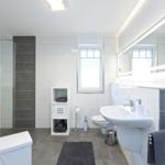 Badezimmer mit Dusche, Waschbecken und Toilette. Graue Fliesen und weißer Einbau.