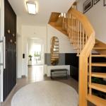 Eingangsbereich mit Holztreppe, runder Teppich und Spiegel an der Wand.