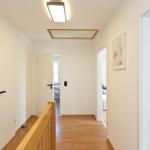 Flur mit Holzboden, weißen Türen und moderner Deckenbeleuchtung. Blick in Schlaf- und Badezimmer.