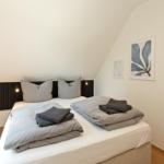 Schlafzimmer mit Doppelbett, grauen Kissen und Kunst an der Wand.