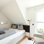 Schlafzimmer mit Dachschrägen, Bett, Sessel und Fenstern.
