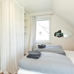 Schlafzimmer mit Dachschrägen, Fenster, Spiegel und Bett mit grauer Bettwäsche.