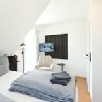 Schlafzimmer mit Bett, Sessel, Fernseher und Wandbildern.