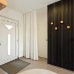 Eingangsbereich mit Holztreppe, weiße Tür und schwarze Holzwand mit runden Knöpfen.