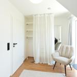 Schlafzimmer mit weißen Wänden, Holzboden und goldener Stehlampe.