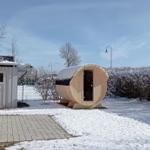 Holzsauna im Schnee vor einem Haus mit Satellitenschüssel und Heizung.