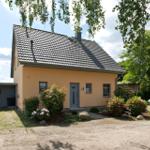 Ein gelbes Haus mit grauem Dach und blühenden Sträuchern im Vorgarten.