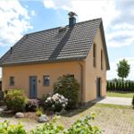 Ein gelbes Haus mit Dach und Garten. Ein Auto steht auf dem Hof.