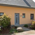 Ein Haus mit gelber Fassade, grauer Tür und einem gepflasterten Weg durch den Garten.