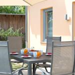 Terrasse mit Esstisch, Stühlen und Sonnenschutz. Auf dem Tisch stehen Tassen und Obst.