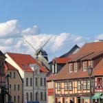 Stadtbild mit historischen Häusern und Windmühle unter blauem Himmel.